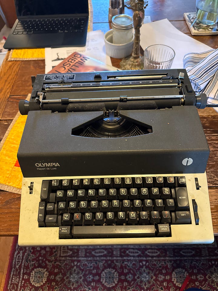 Two electric typewriters, one a black-and-cream-colored Olympia, one a caramel-colored Brother Coronet
