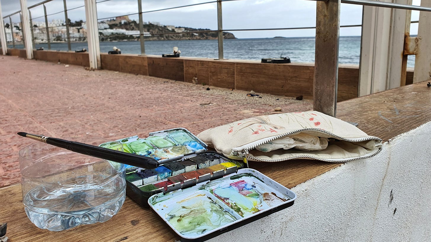 A water pot, a paintbrush, a plein air watercolour set and pencil case ona  wall in a quiet spot in Ibiza