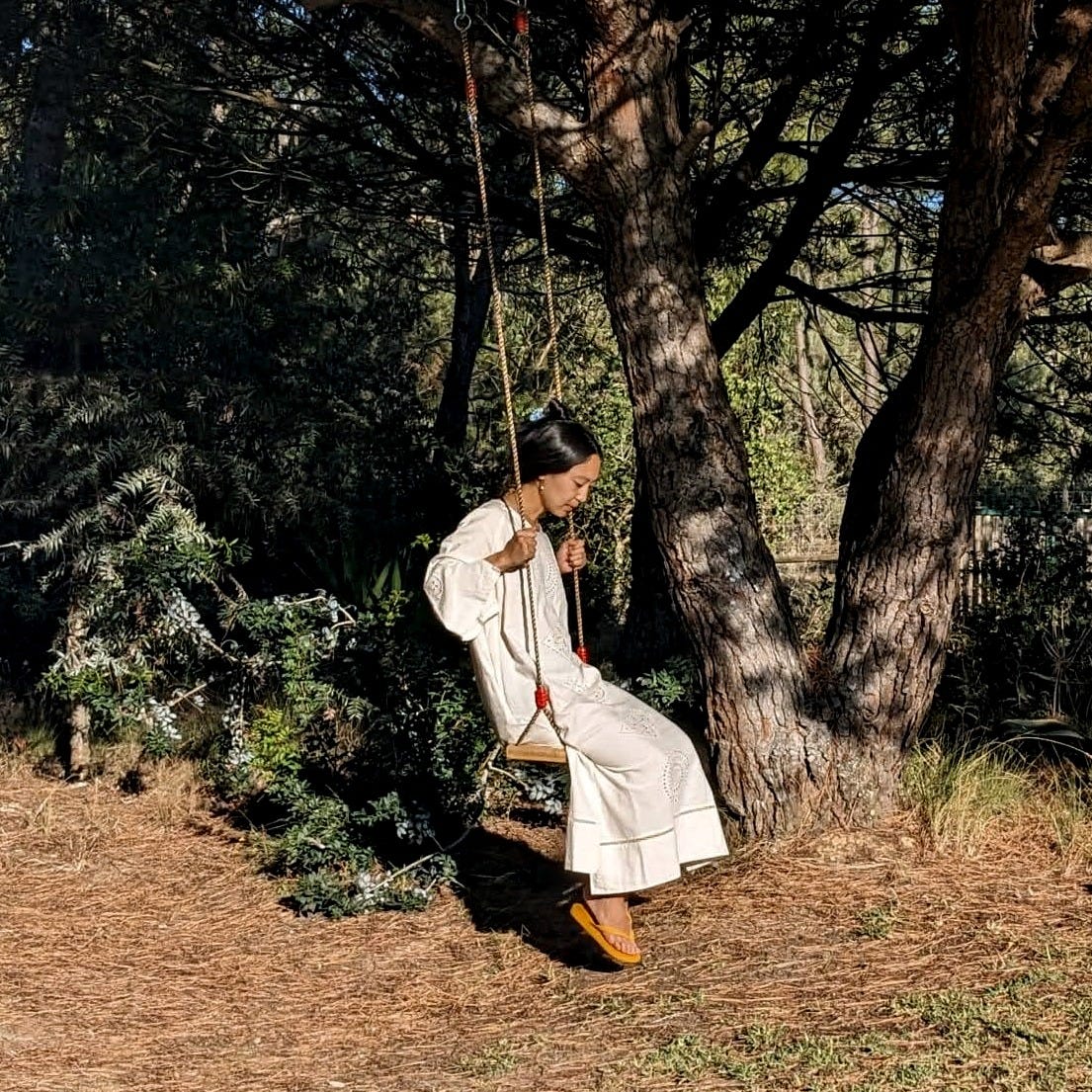 Photo of a person in a long white dress on a swing hanging from a tree branch.