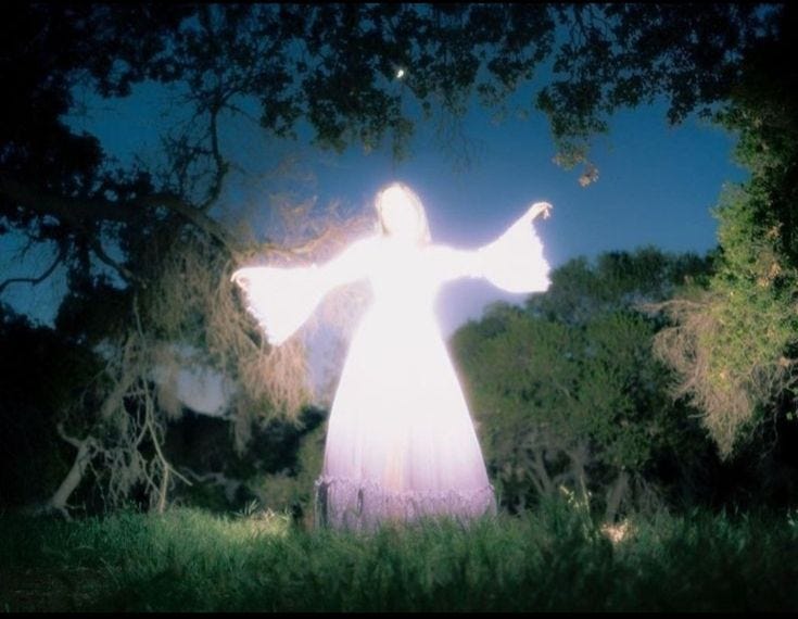 This may contain: a person standing in the grass with their arms spread out and lights shining on them