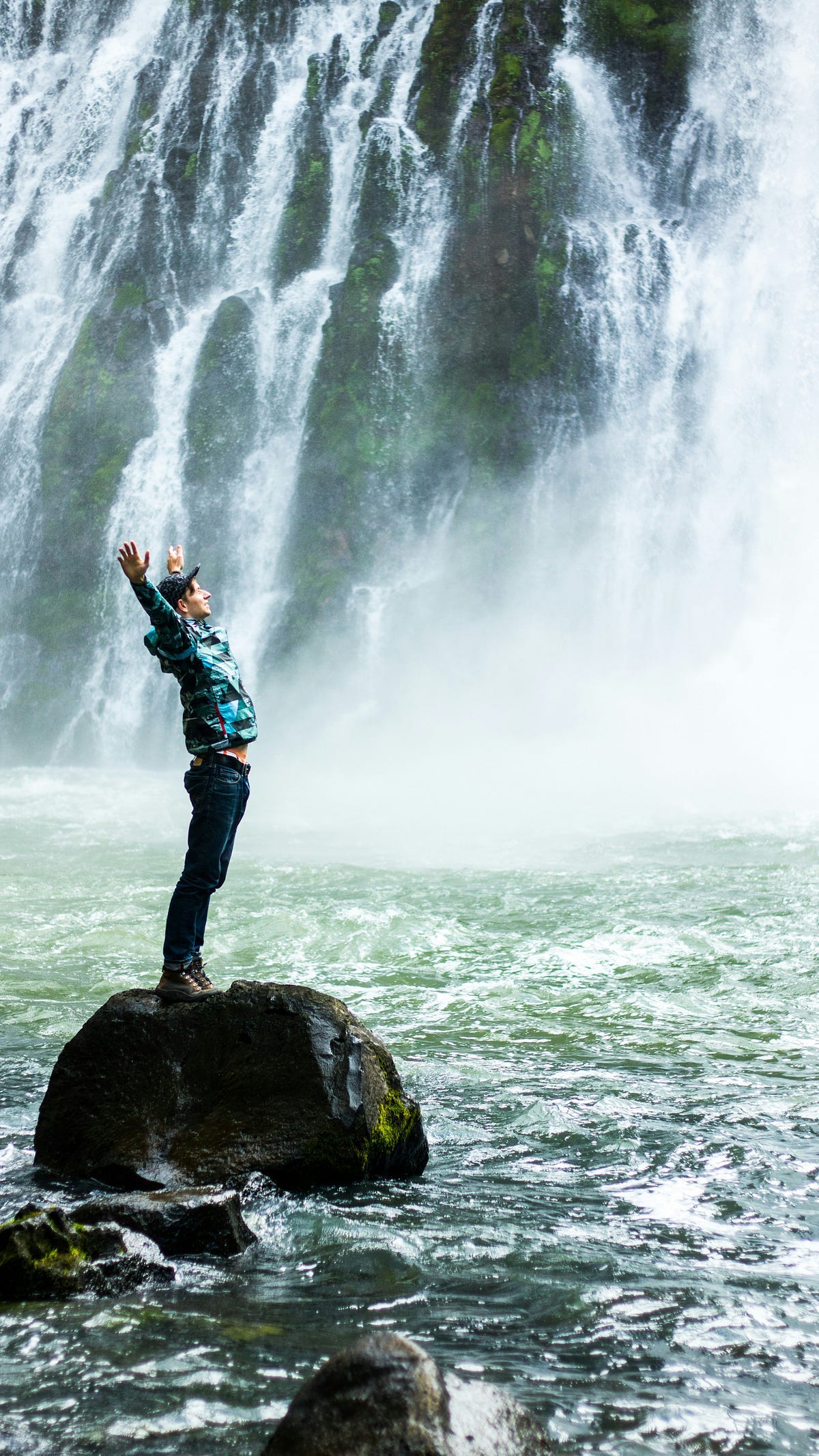 Person looking at a waterfall with raised hands.