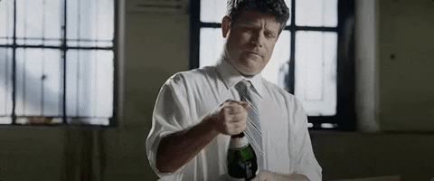 Funny reaction image of a man in a shirt and tie holding a champagne bottle, used in Beating The Tide’s free cash flow yield article to celebrate spotting strong stock investing opportunities and avoiding value traps.