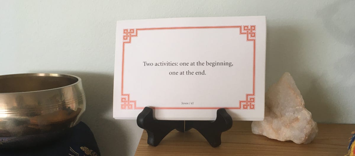 Lojong card that reads “Two activities: one at the beginning, one at the end” sitting on a wooden shrine with an unpolished chunk of quartz to the right and a meditation bowl to the left.