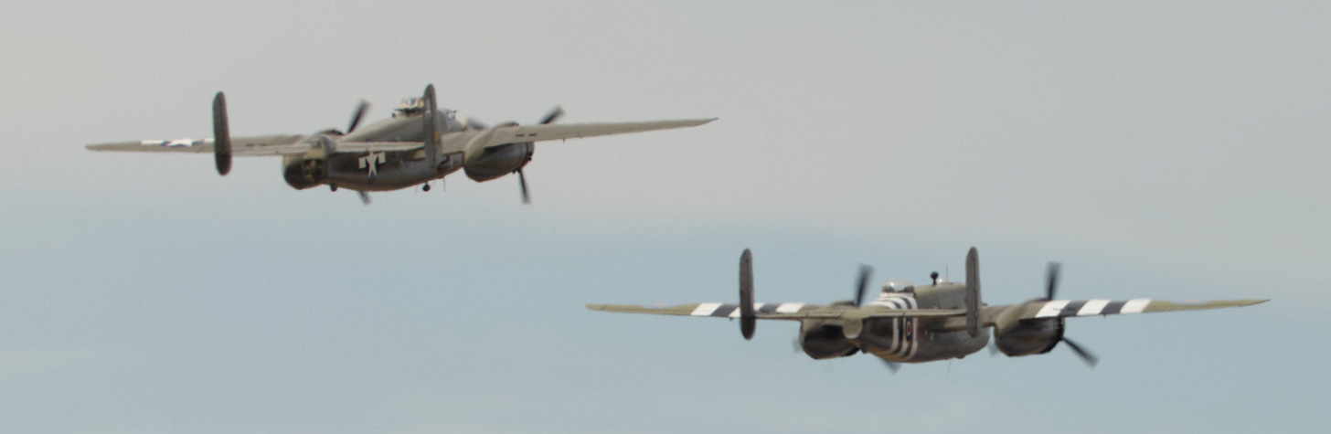Two dual-propeller planes fly away from the camera in a clear sky.