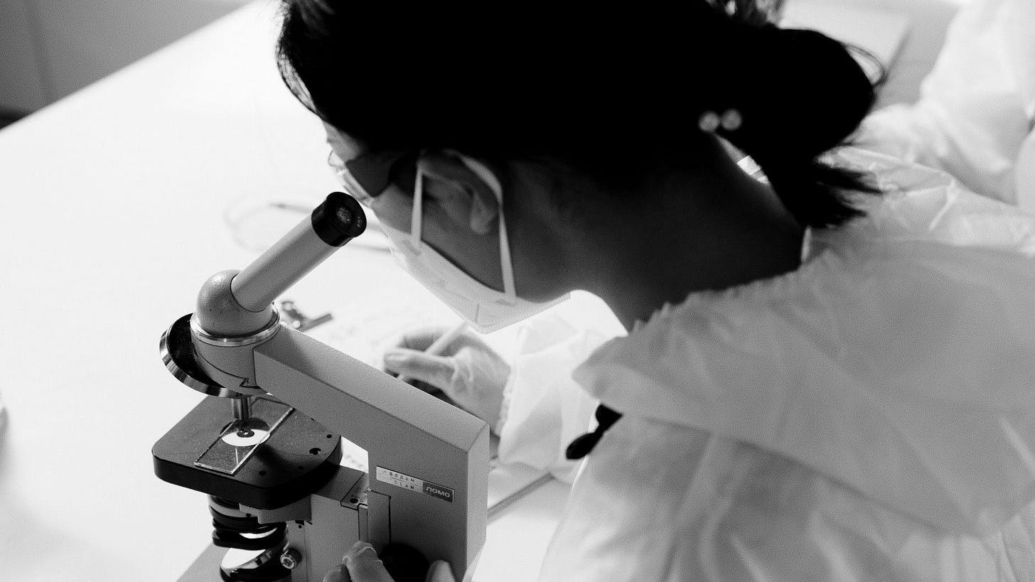 Photo by Artem Podrez on Pexels Black and white image of a scientist examining through a microscope wearing a facemask and protective goggles. (stock photo)