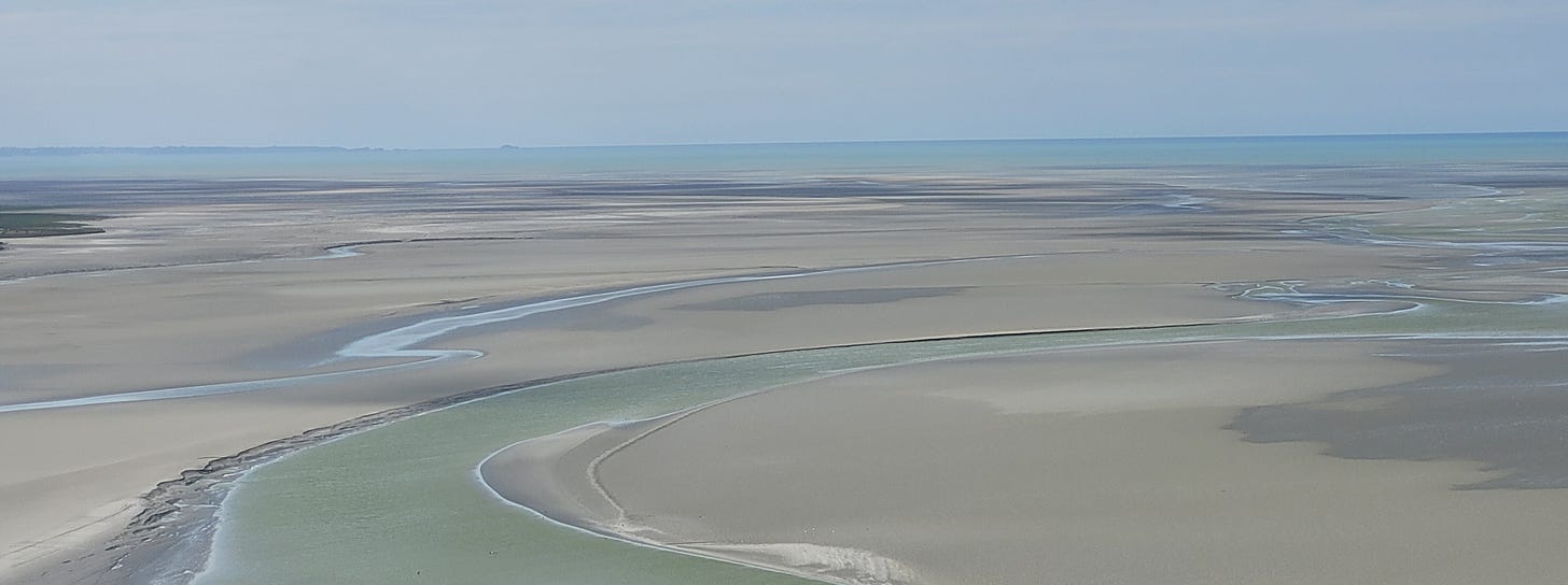 A photo of the estuary at Mont St-Michel. the tide is out and the sand stretches to the far horizon.