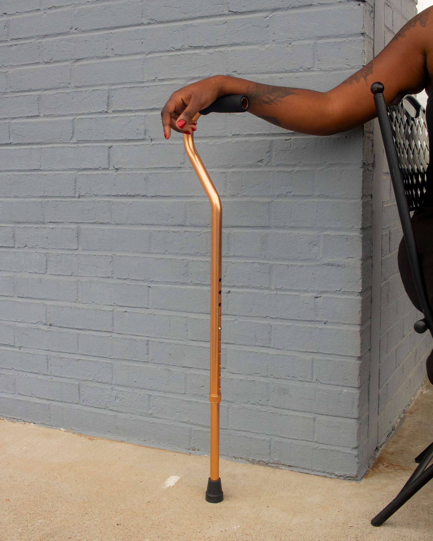 Photo of the author's tattooed arm supporting her gold cane in front of a brick wall. Photo of the author's tattooed arm supporting her gold cane in front of a brick wall.