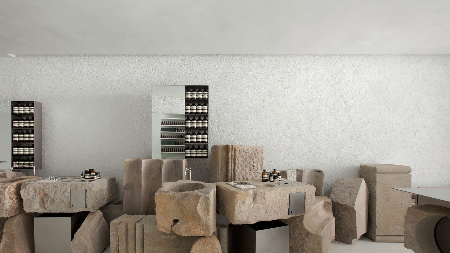 Aesop Diagonal store interior, carved stone basin and metal shelving displaying rows of amber bottles.