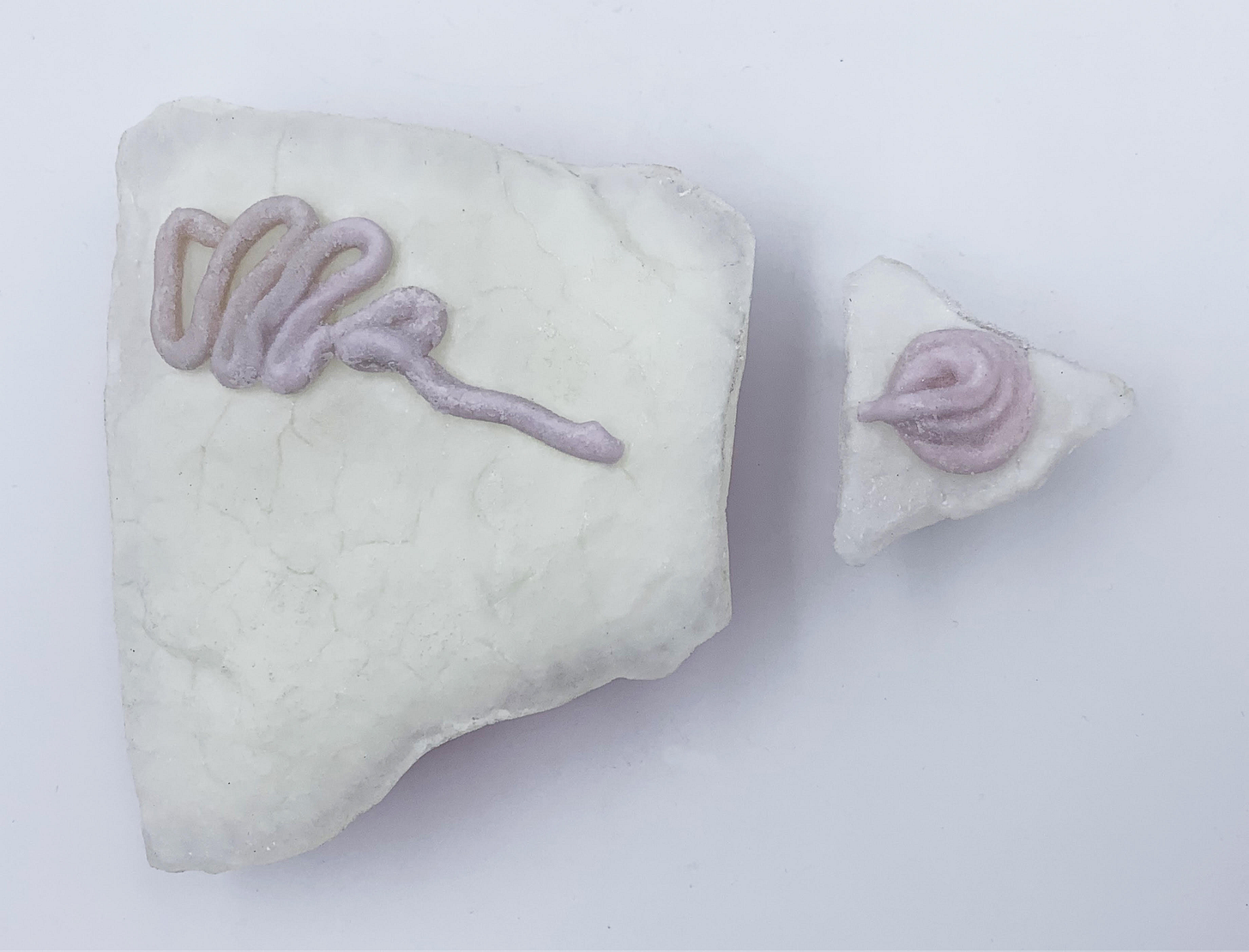 An abstract, two-part sculpture, white, with lavendar squiggles on top of each piece. Glass sculpture by Megan Biddle.