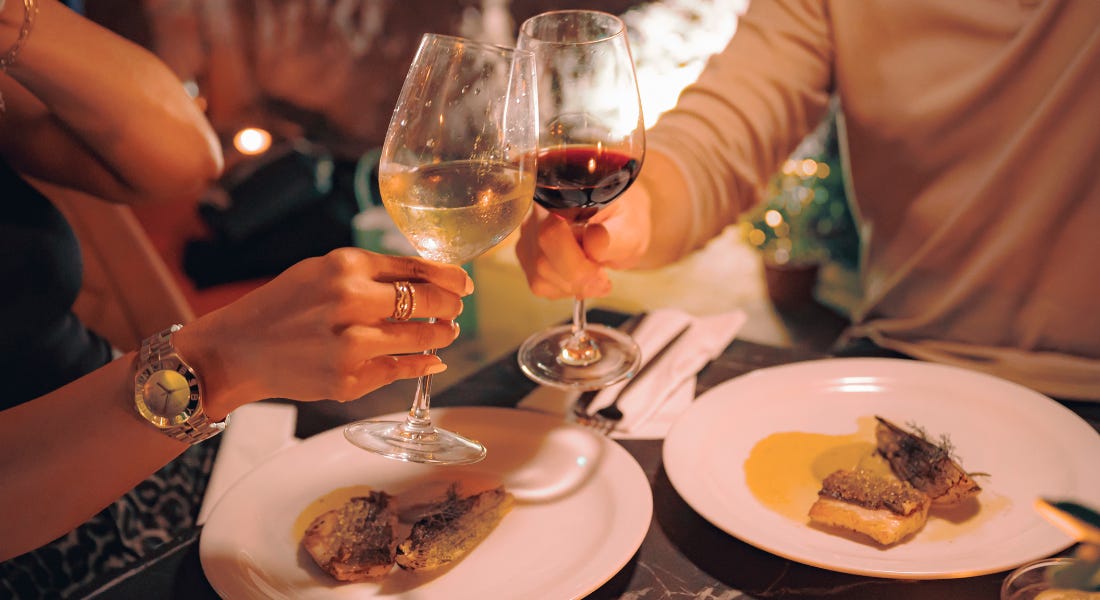 Two wine glasses being clinked together with plates of food underneath them Two wine glasses being clinked together with plates of food underneath them