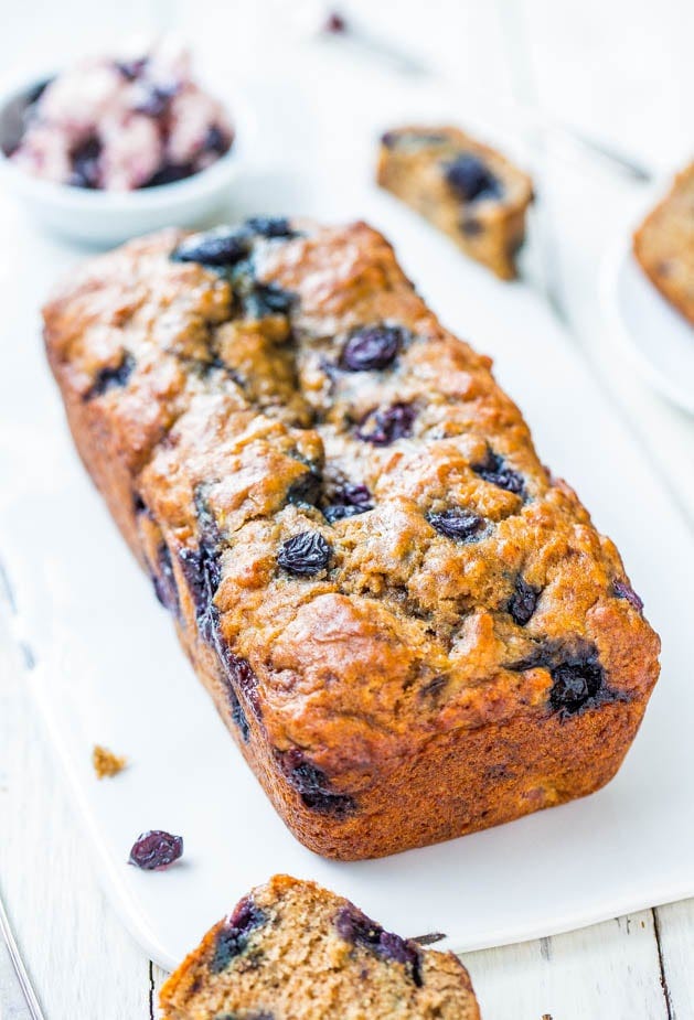 A freshly baked blueberry loaf cake on a white serving platter with scattered blueberries around it. A freshly baked blueberry loaf cake on a white serving platter with scattered blueberries around it.
