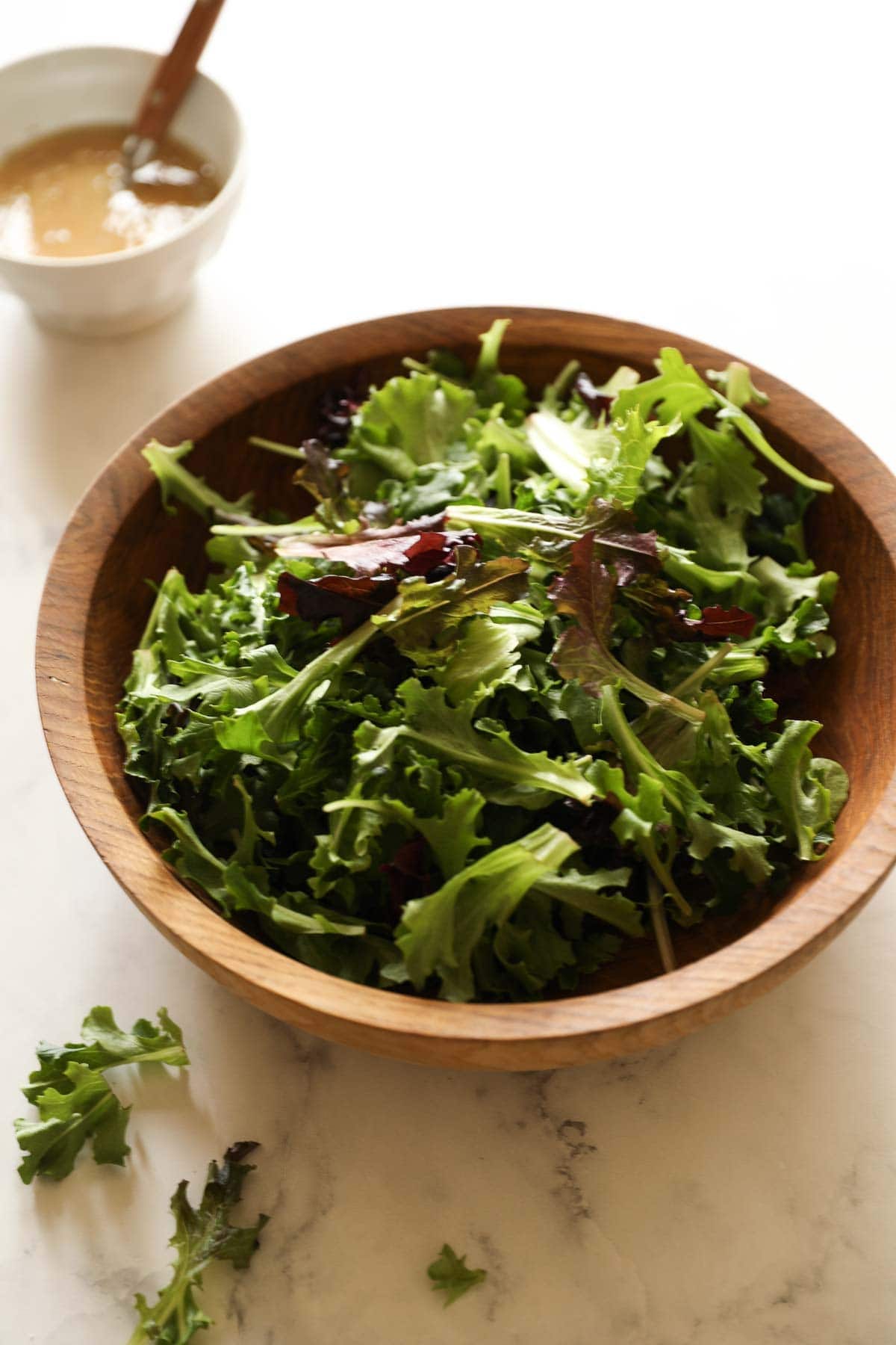 a salad bowl with tossed greens and a bowl of vinaigrette