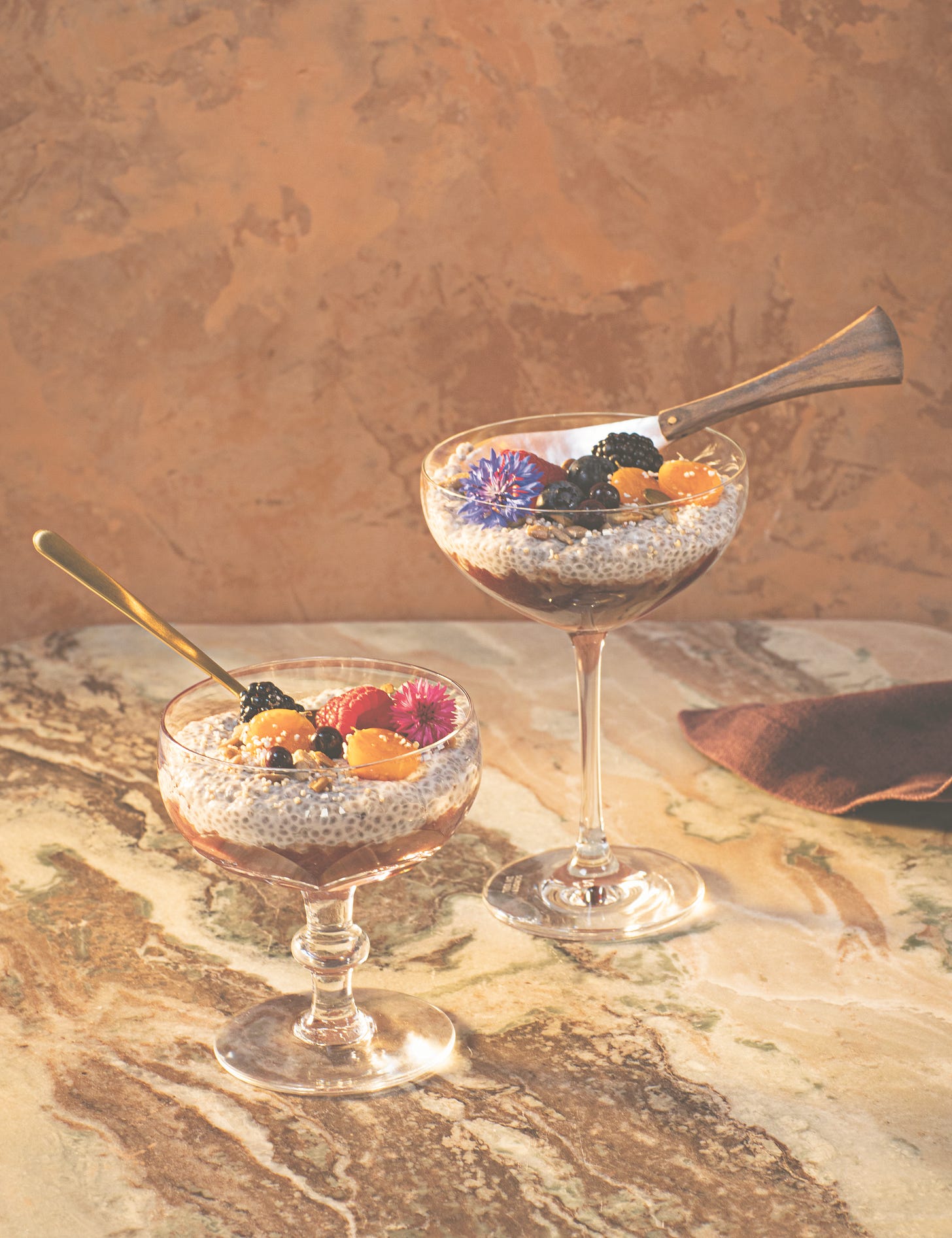 two cocktail glasses filled with pudding, fruit and fresh flowers