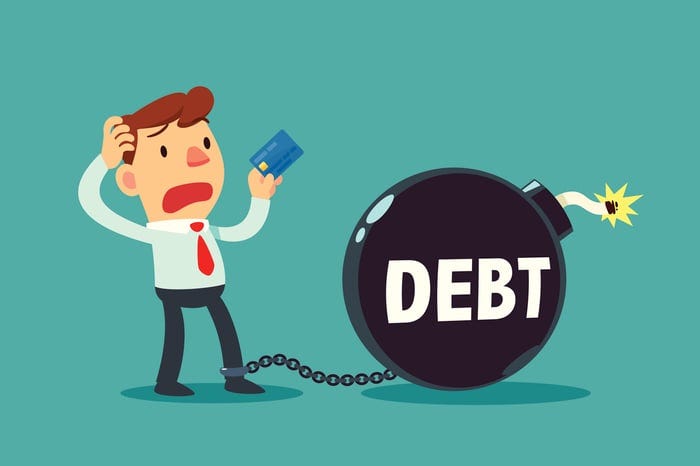 A cartoon man in a suit chained to a debt time bomb and holding a credit card.