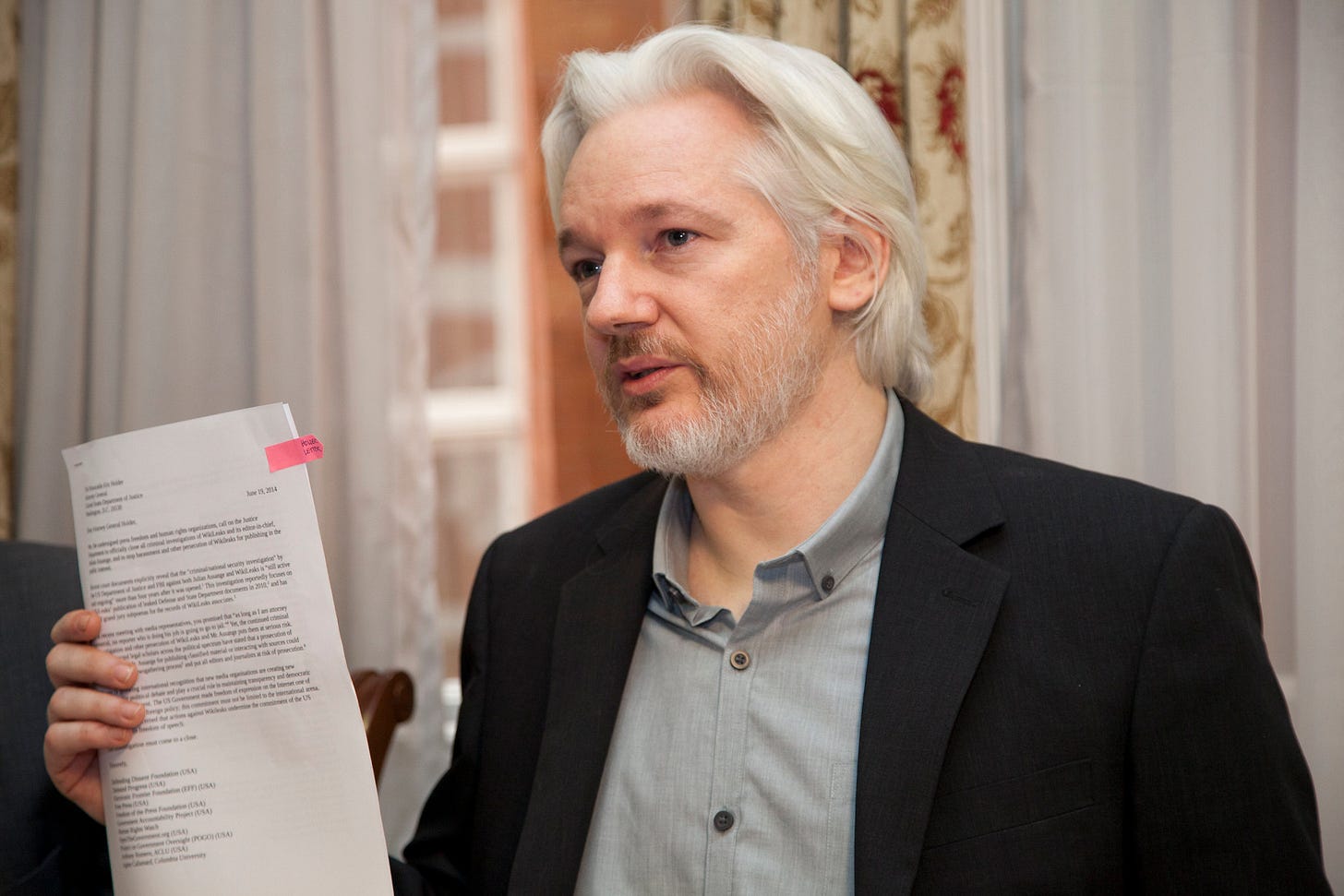 WikiLeaks co-founder and publisher Julian Assange holds a stack of documents during a press event. He's wearing a gray shirt and black suit coat. WikiLeaks co-founder and publisher Julian Assange holds a stack of documents during a press event. He's wearing a gray shirt and black suit coat.