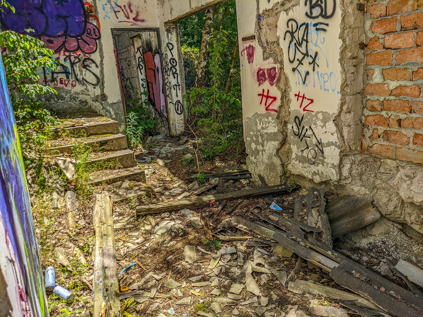 A ruined building with the roof gone, walls shattered and graffiti covering the concrete walls while detritus covers the ground.