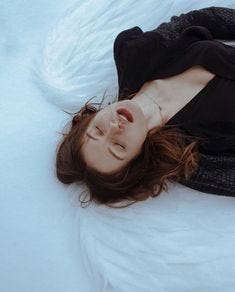 This may contain: a woman laying on top of a bed covered in white sheets and blankets with her eyes closed