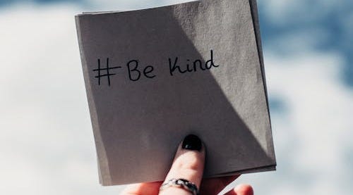 Free A hand holding a note with '#Be kind' inscribed, set against a bright sky. Stock Photo Free A hand holding a note with '#Be kind' inscribed, set against a bright sky. Stock Photo