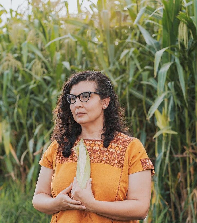 Denise standing in a corn field holding an ear of corn