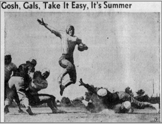 A black-and-white newspaper photo of a woman leaping in the air carrying a football in her left hand and with her right arm outstretched. She is wearing a fitted long-sleeve football uniform with pads and a 1940s helmet sans facemask or strap, and jumping over a pile of similarly-uniformed women who are trying to tackle her or block for her. The title of the photo reads, “Gosh, Gals, Take It Easy, It’s Summer.” 