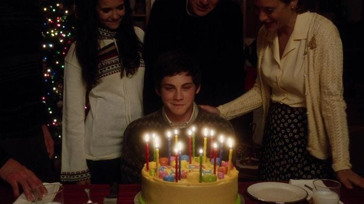 This may contain: a young man sitting in front of a birthday cake with lit candles on top of it
