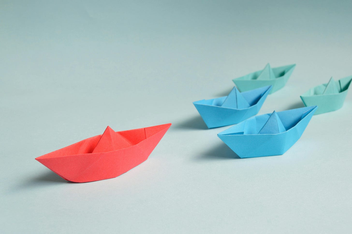 Little paper boats with one in red leading at the top