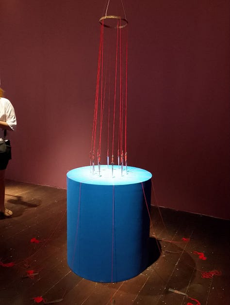 Grade de imagens da exposição, com muitos fios vermelhos e objetos cortantes e pontiagudos como serrote, foice, agulhas e adagas.