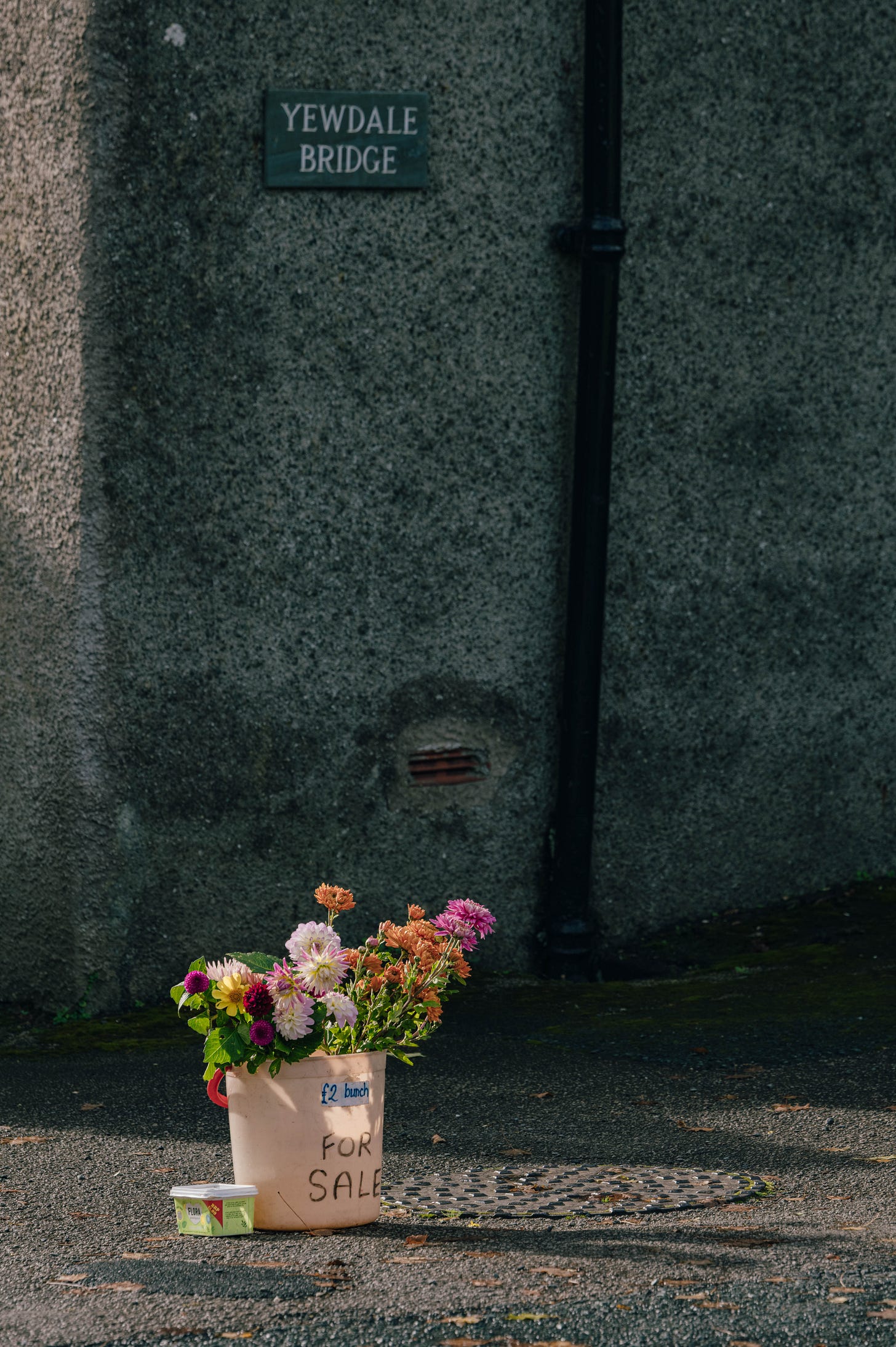 Small roadside flower bucket for sale near Coniston in the Lake District, England, rural village scene. Small roadside flower bucket for sale near Coniston in the Lake District, England, rural village scene.