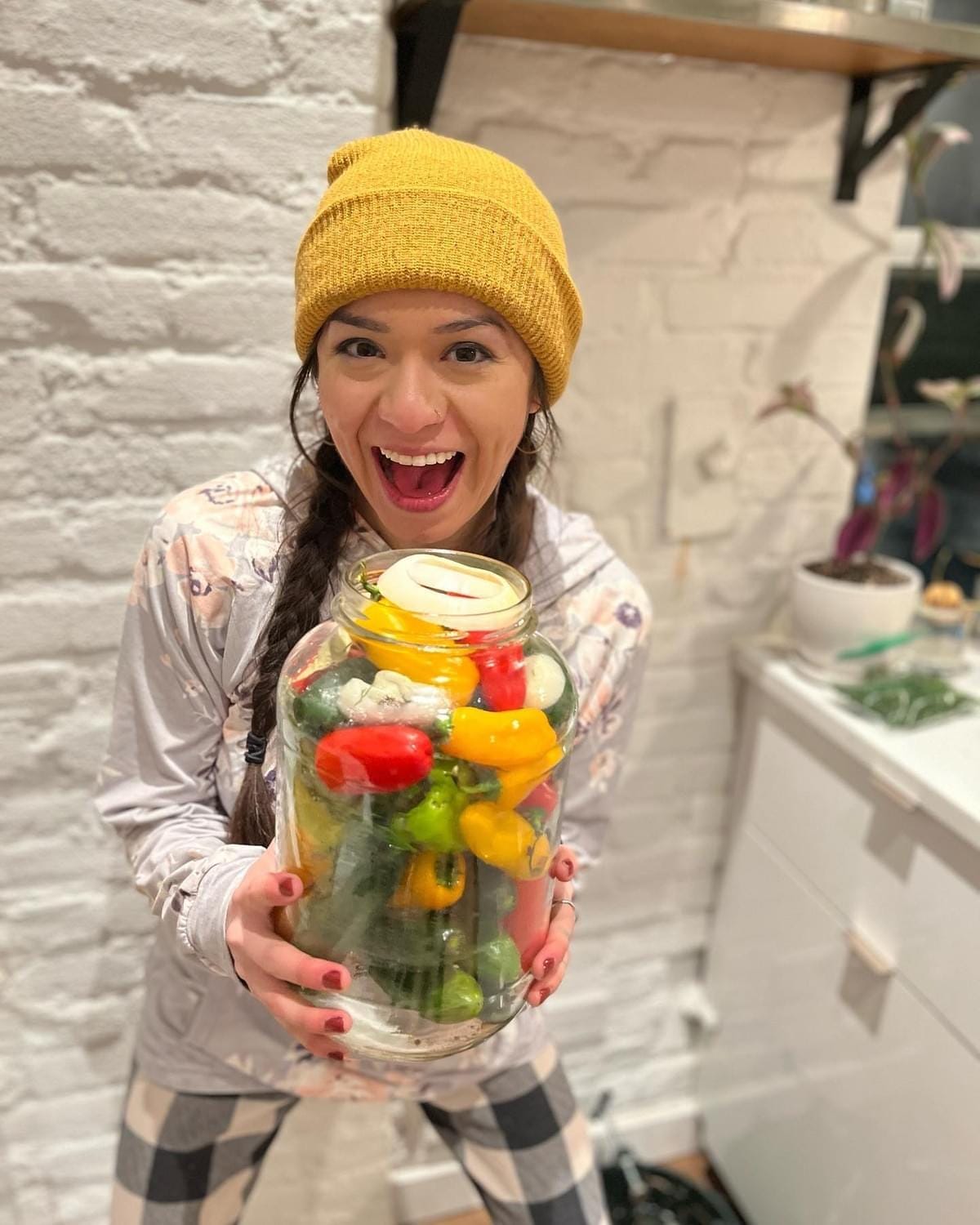 photo of a woman smiling at the camera while holding a large jar of peppers about to be pickled