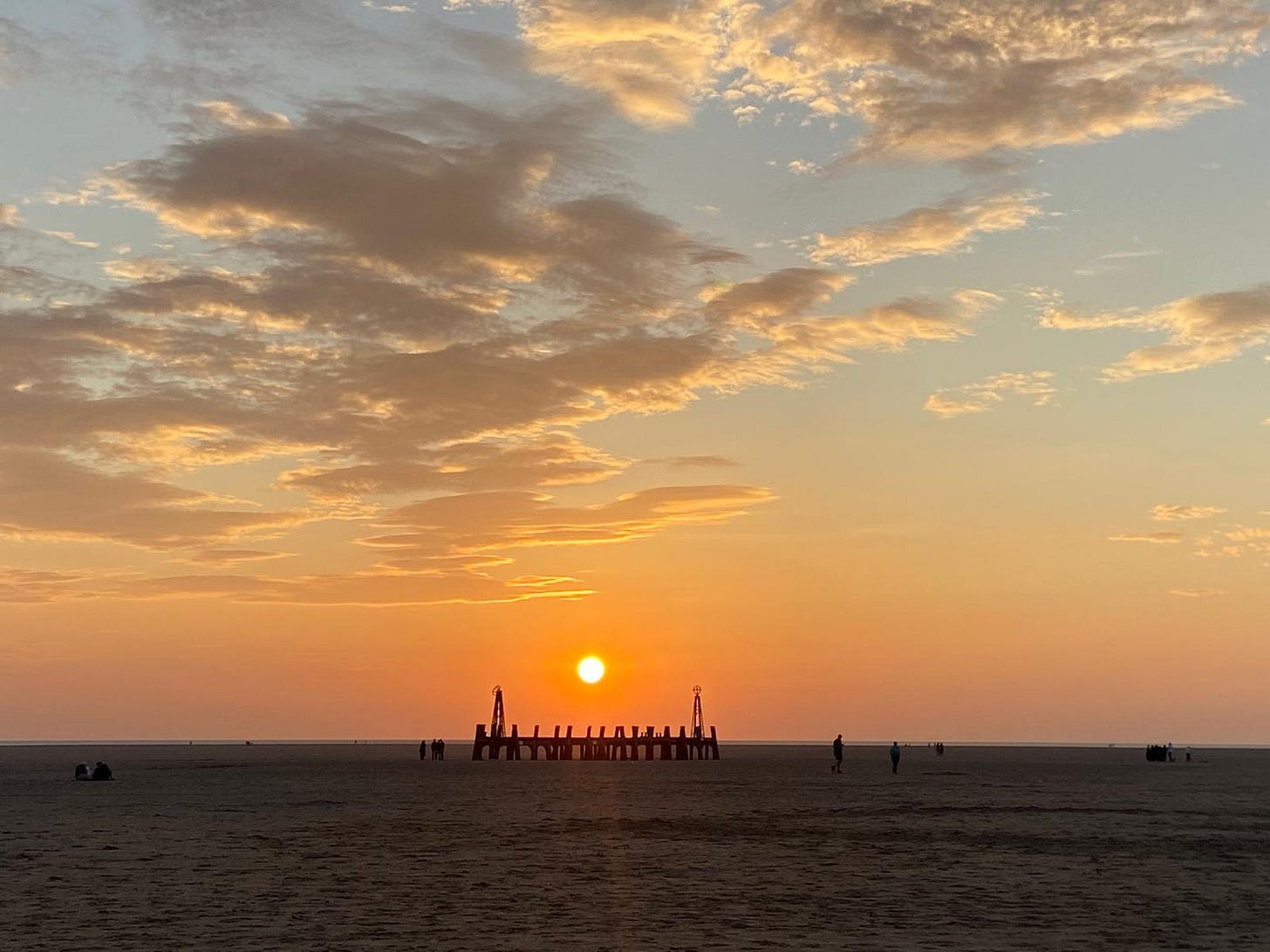sandy beach with burnt end of a pier and orange round sun above it