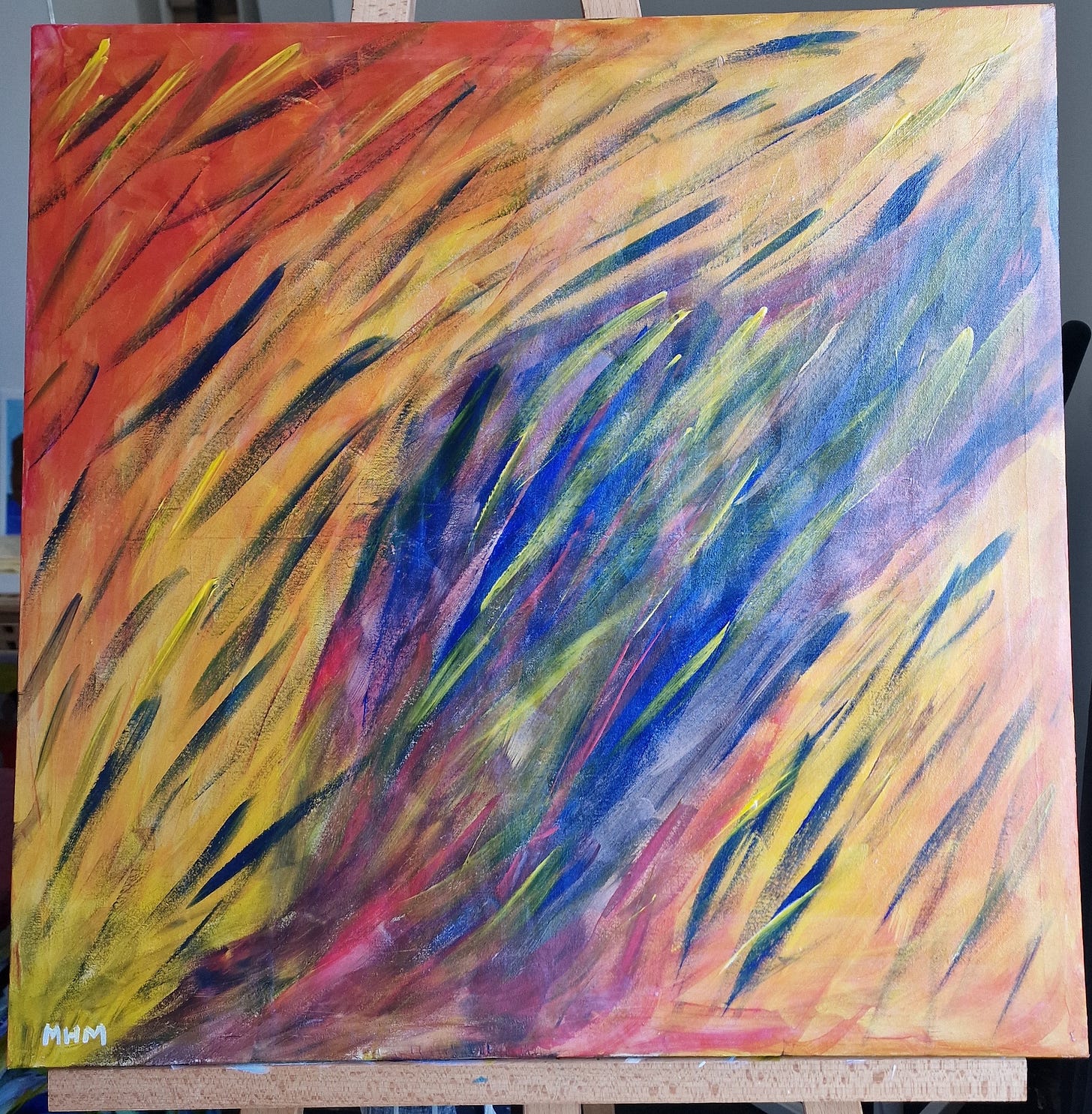 Abstract art on a canvas - the main background colour is red that merges into orange and yellow with a motion of movement from bottom left to upper right represented by highlighted flecks of varying shades of yellow, blue, green, red, and purple colours. The centre of the canvas has a background of deep purple changing to red, yellow, blue and green as it merges with the adjacent yellow, orange and red colours. Bottom left of the canvas bears my initials: MHM.