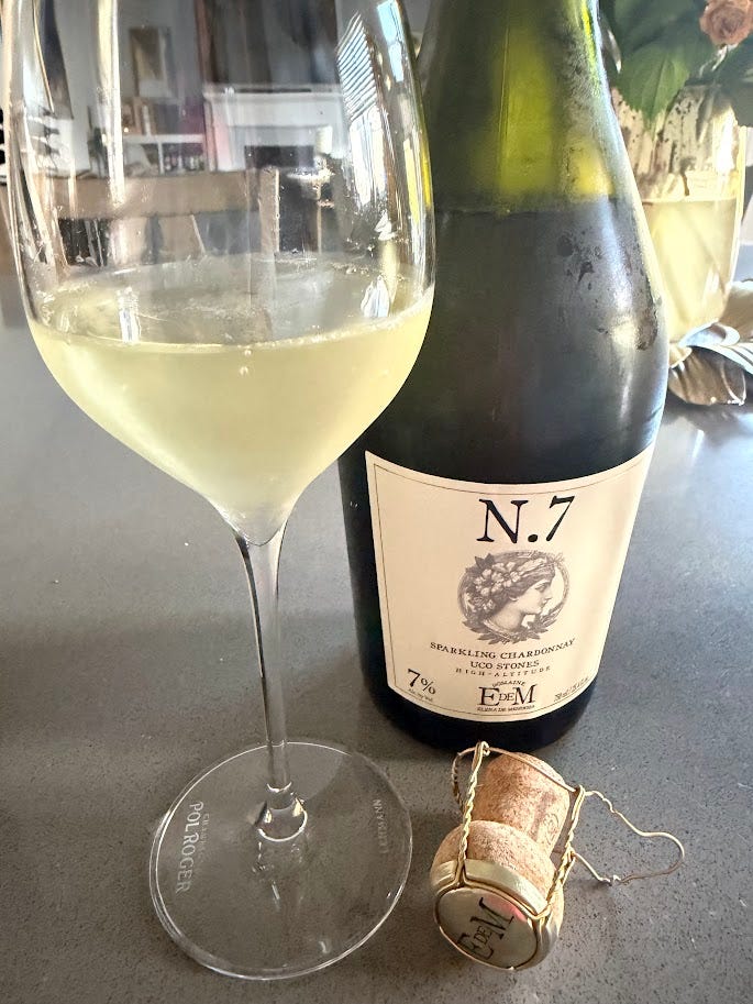Two Domaine EdeM sparkling Chardonnays poured at home: the N.7 Uco Stones, pale gold in a stemmed glass beside its cork, and the golden-hued Blonde, non-alcoholic, poured beside a Peugeot wine preserver.