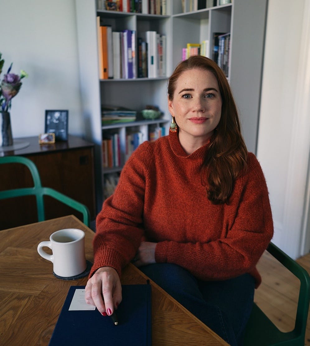 a woman in a red jumper sitting at a table looking at the camera