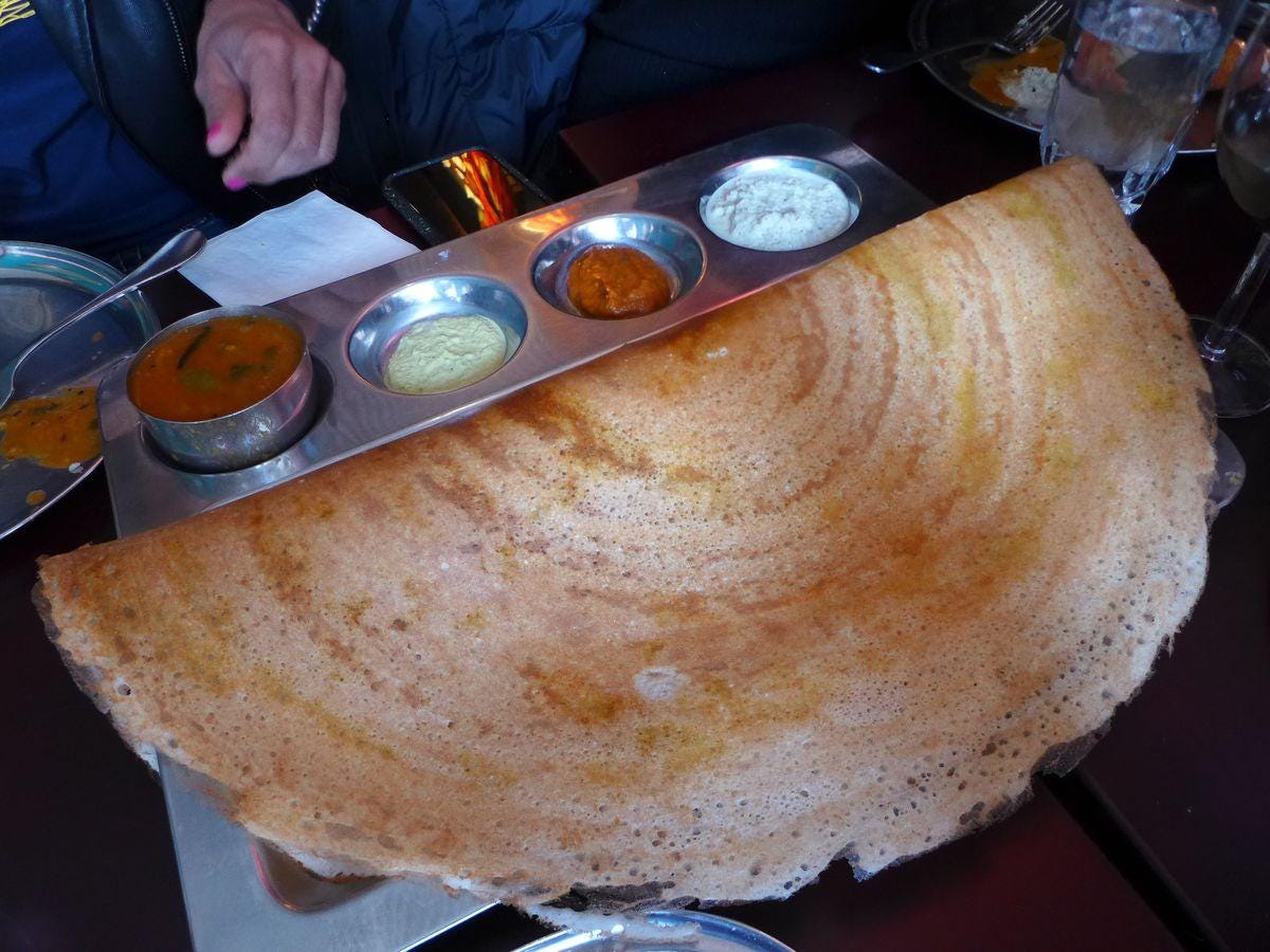A crescent shaped dosa with four sauces.
