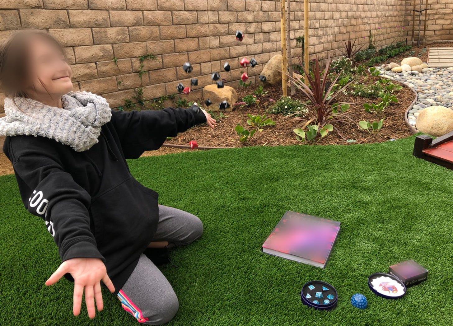 Pre-teen girl wearing a black hoodie and fuzzy grey infinity scarf smiles as she tosses rpg dice in the air.