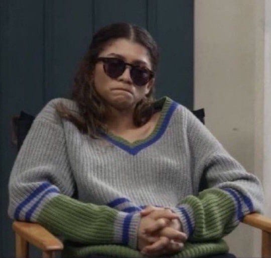 This may contain: a woman sitting in a chair with her hand on her chest and wearing sunglasses over her face