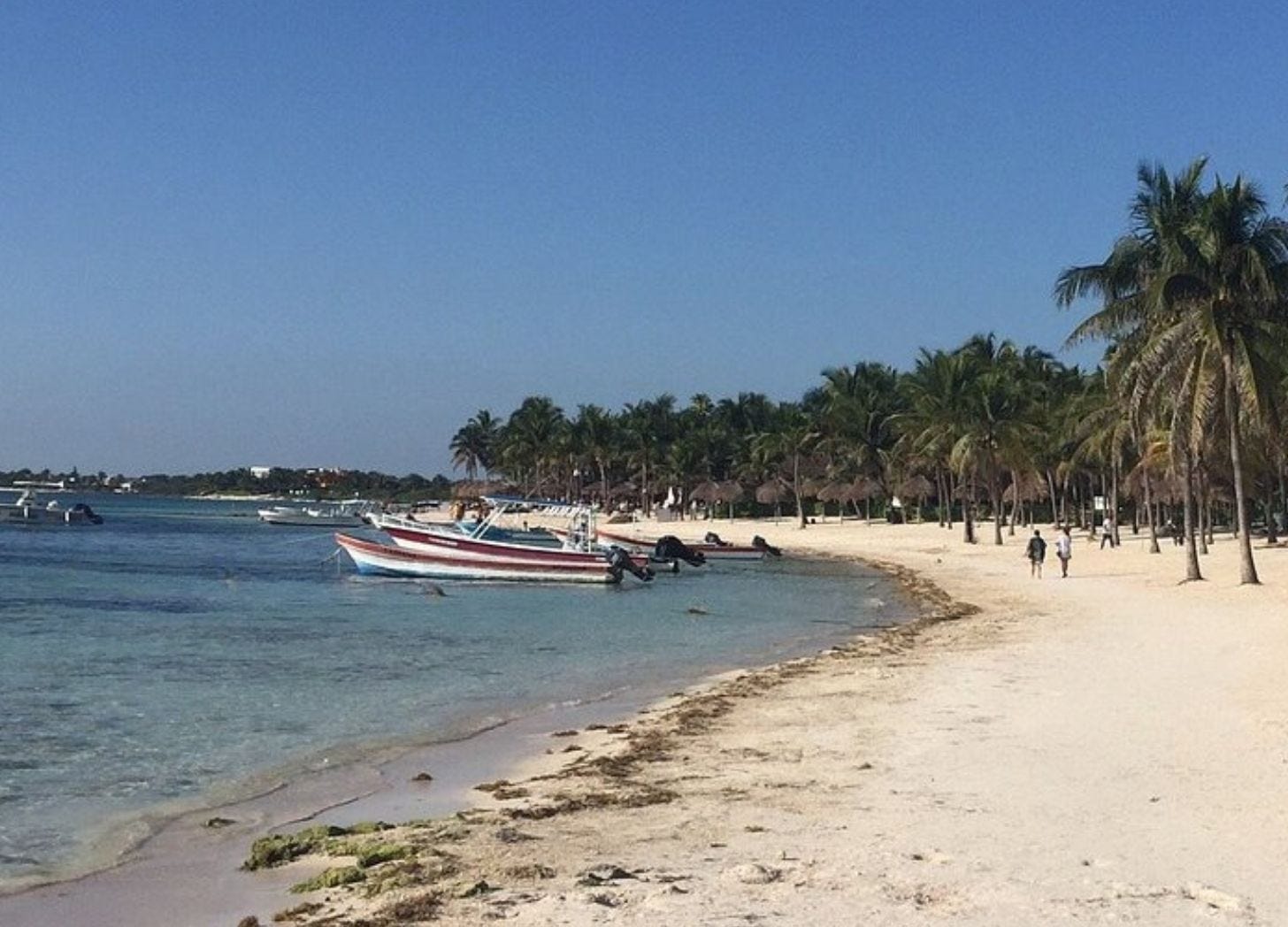 Akumal Bay on a sunny day. Fishing pangas anchored in shallow turquoise water just off a white sand beach lined with palm trees. Akumal Bay on a sunny day. Fishing pangas anchored in shallow turquoise water just off a white sand beach lined with palm trees.
