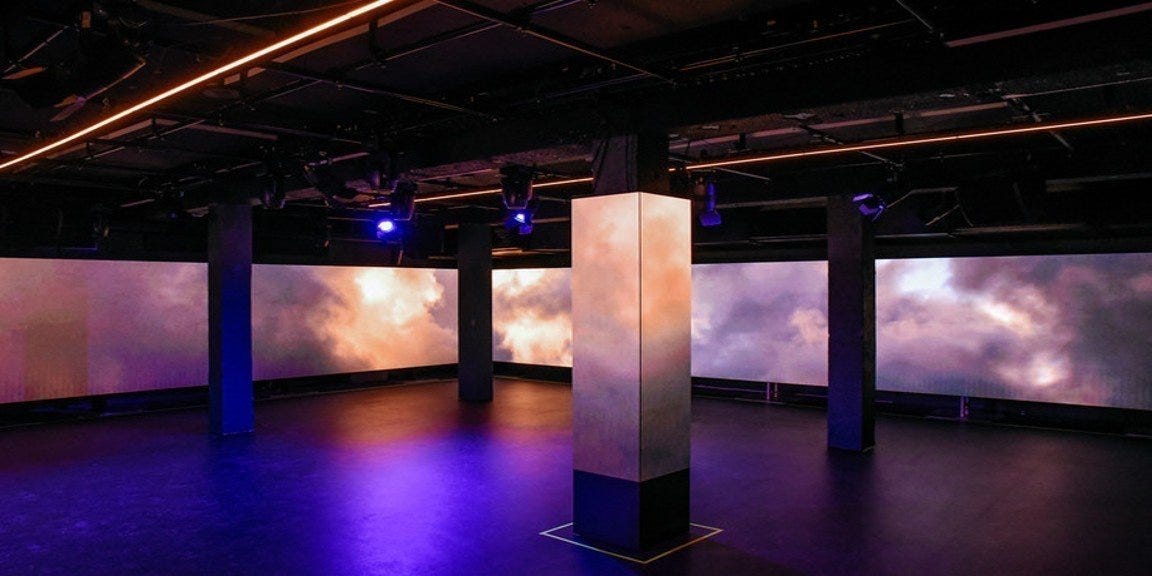 An immersive performance space featuring a large wraparound LED screen setup with multiple digital displays along the walls and pillars. An immersive performance space featuring a large wraparound LED screen setup with multiple digital displays along the walls and pillars.