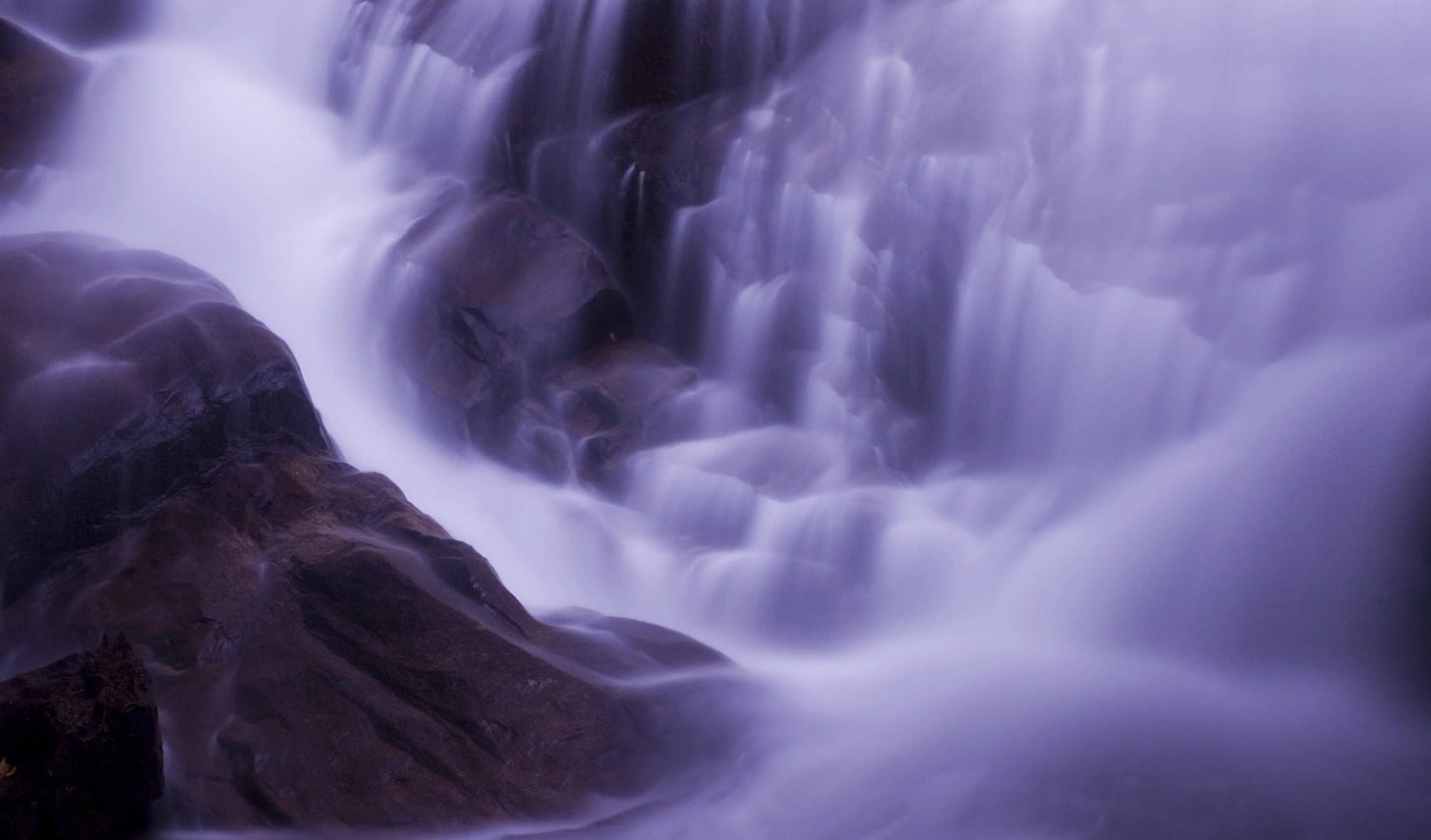 Long exposure of a waterfall pounding onto purple rocks rocks