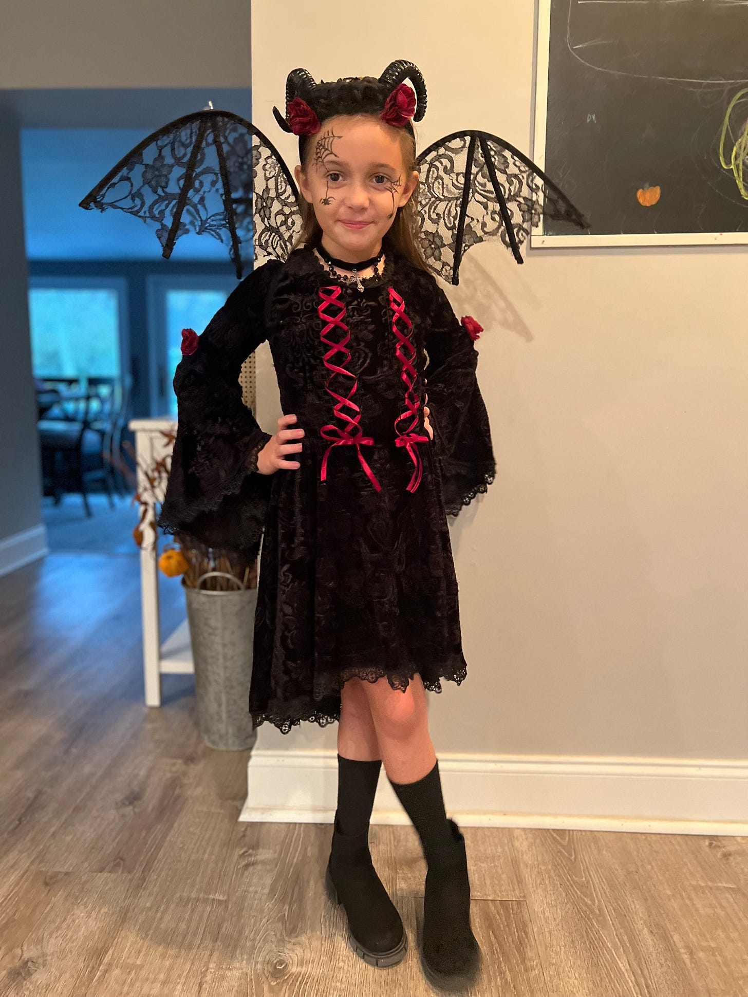 Young girl dressed in a black lace dress, with lacey black wings and black devil horns.