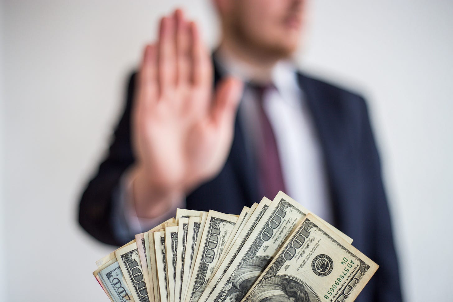 A man's hand being put up to say NO to several hundred dollar bills being offered