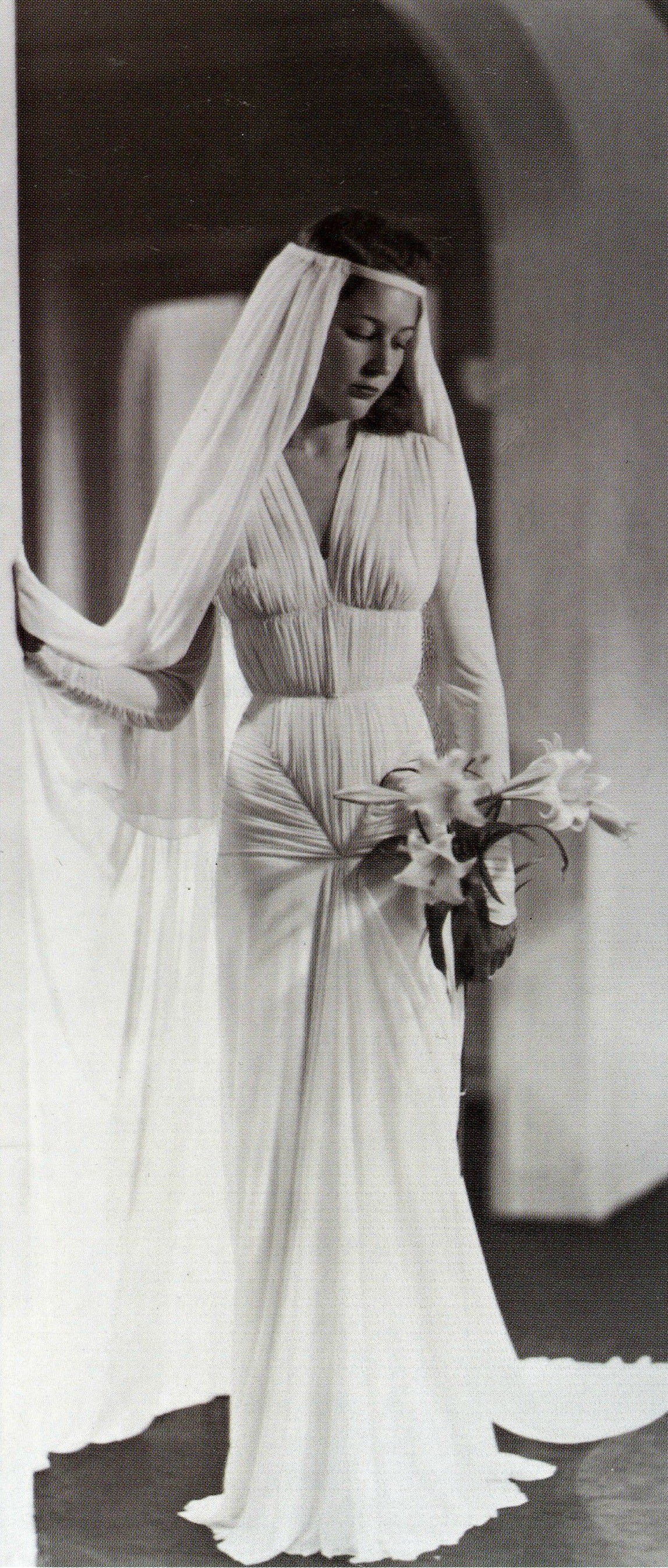 A bride with long veil wears a densley pleated white dress while holding white callas lillies.