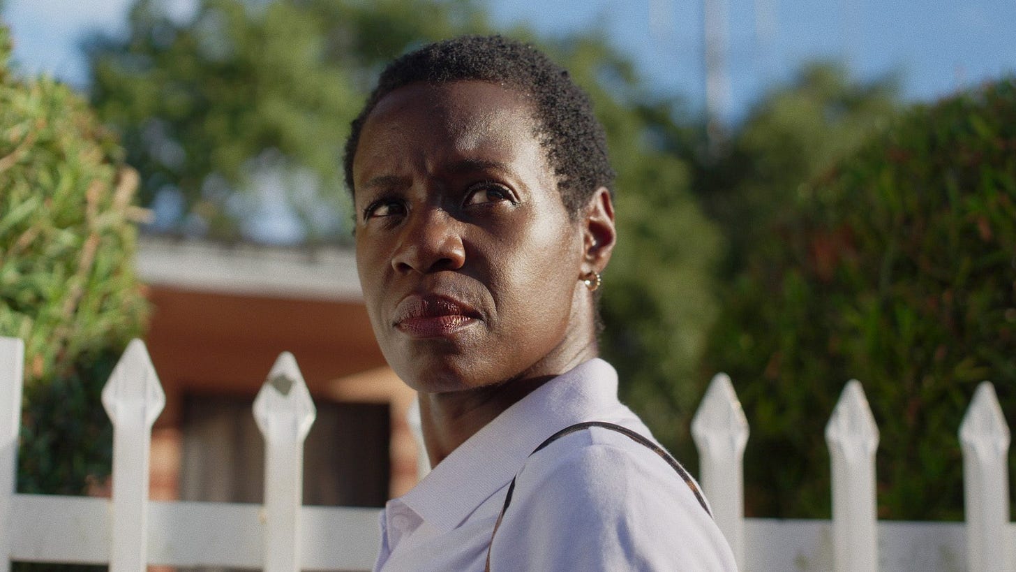 Woman looking off in the distance with a white picket fence behind her.