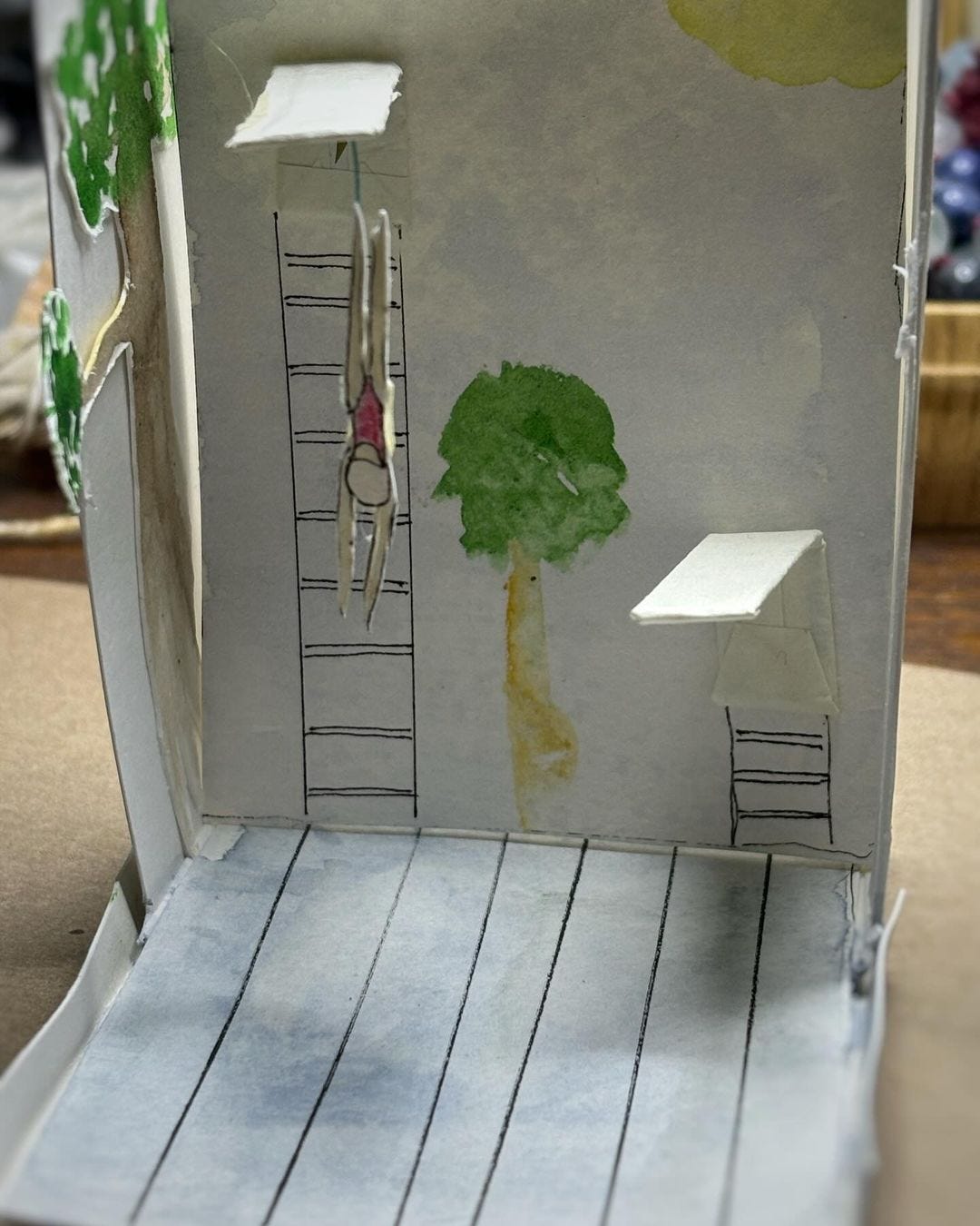 Image of a small diorama of a pool with two diving boards and a figure in a red bathing suit diving from the high board.