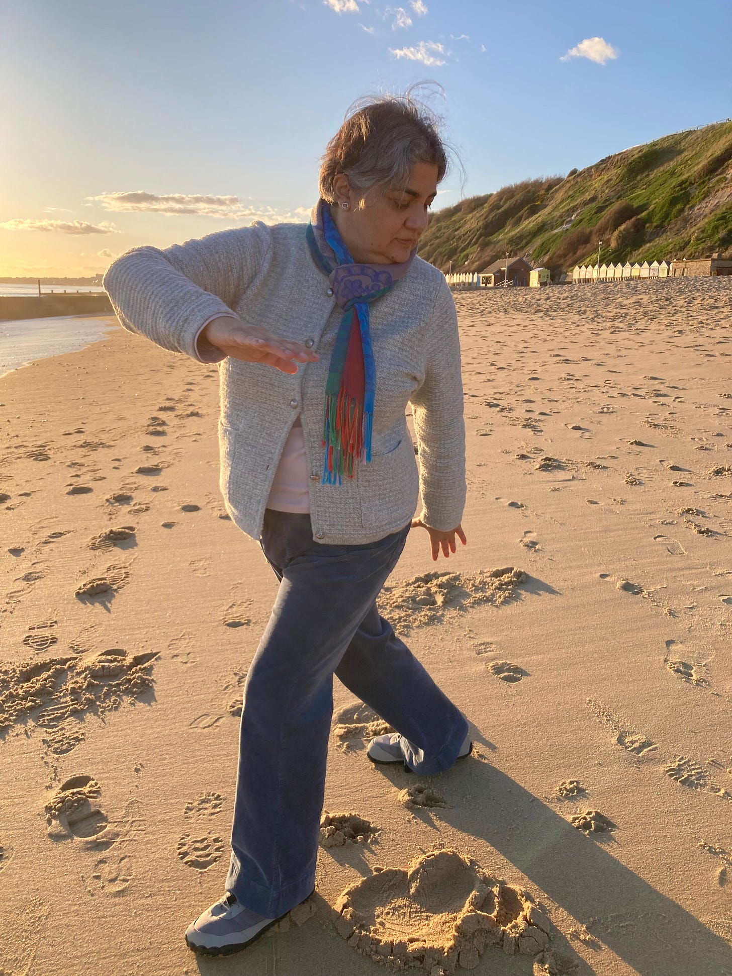 Rakhee Jasani practicing Qigong on the beach with the sea and cliffs in the background