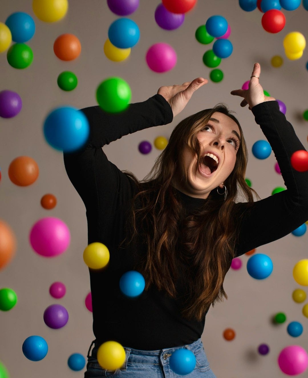 a woman in a black shirt and jeans is surrounded by balloons a woman in a black shirt and jeans is surrounded by balloons