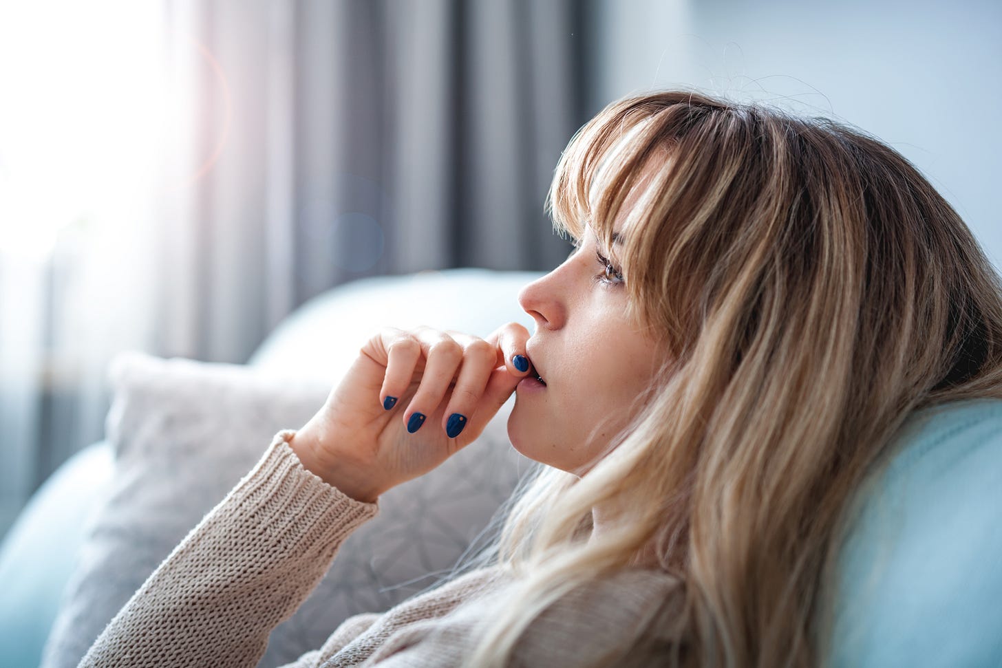 A woman stares pensively into the distance while she chews her nails.