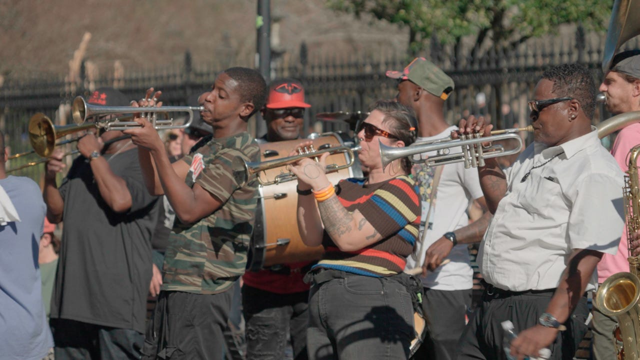 A group of musicians play brass instruments on the street. A group of musicians play brass instruments on the street.