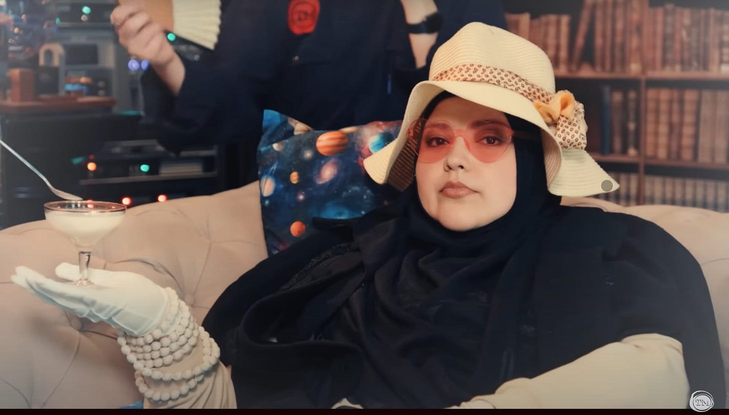 Fatiha El-Ghorri lounges on a sofa holding a martini glass of yogurt. She is wearing a hajib, a straw hat, and rose-colored heart-shaped glasses.