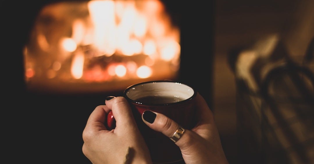 a woman holding a cup of coffee in front of a fireplace